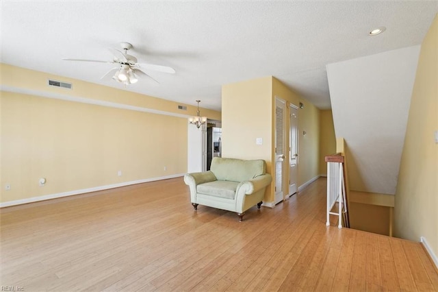 unfurnished room with visible vents, baseboards, light wood-type flooring, an upstairs landing, and ceiling fan with notable chandelier