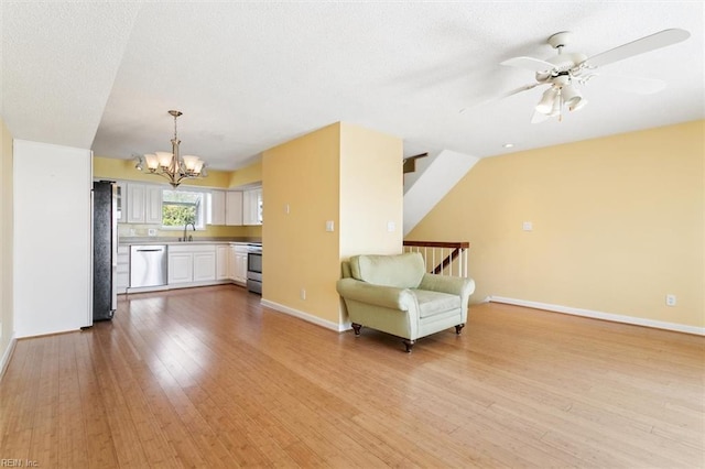 unfurnished room with ceiling fan with notable chandelier, baseboards, light wood-style floors, and a sink