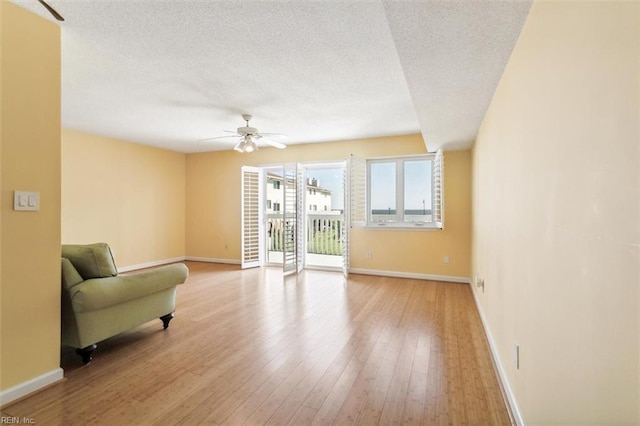 sitting room with baseboards, a textured ceiling, light wood-style floors, and a ceiling fan