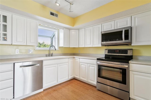 kitchen featuring visible vents, a sink, white cabinetry, stainless steel appliances, and light wood finished floors