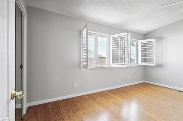 spare room featuring a textured ceiling, baseboards, and hardwood / wood-style floors