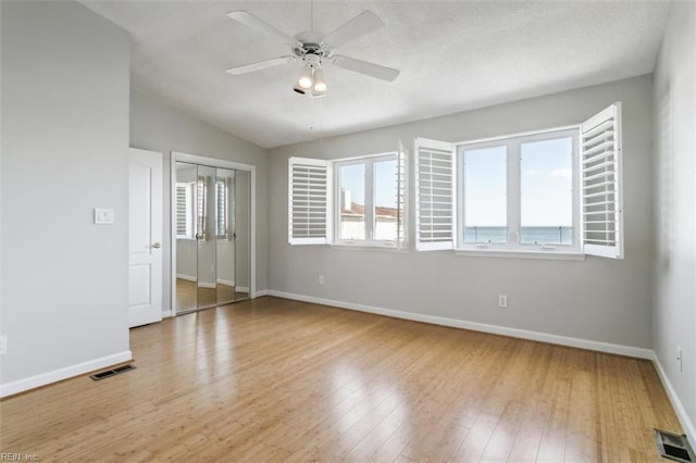 empty room with lofted ceiling, a ceiling fan, visible vents, and light wood-type flooring