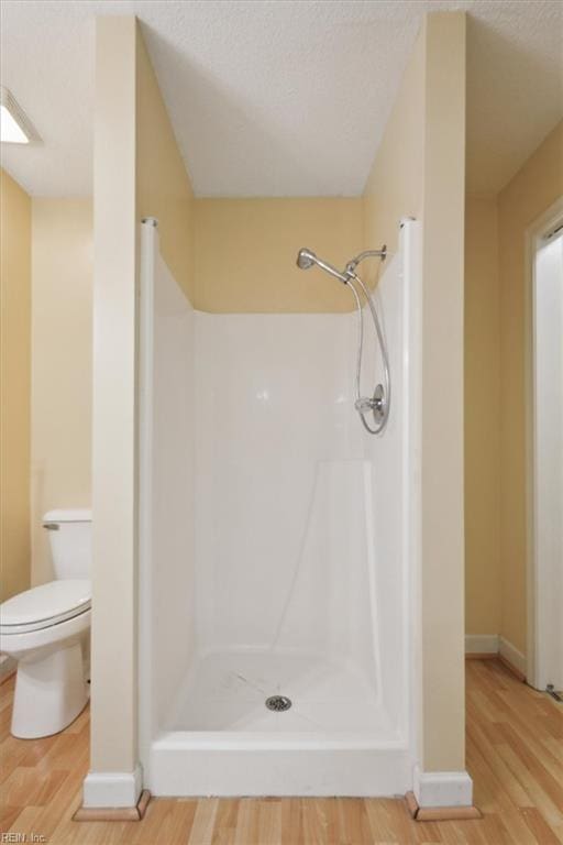 full bathroom featuring wood finished floors, baseboards, a shower stall, a textured ceiling, and toilet