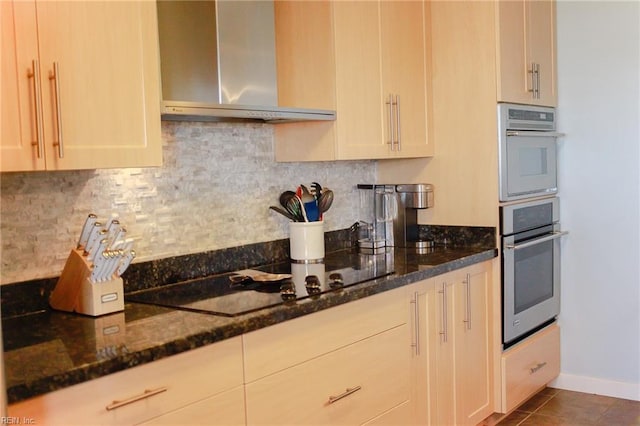 kitchen with wall chimney range hood, backsplash, black electric cooktop, and dark stone counters