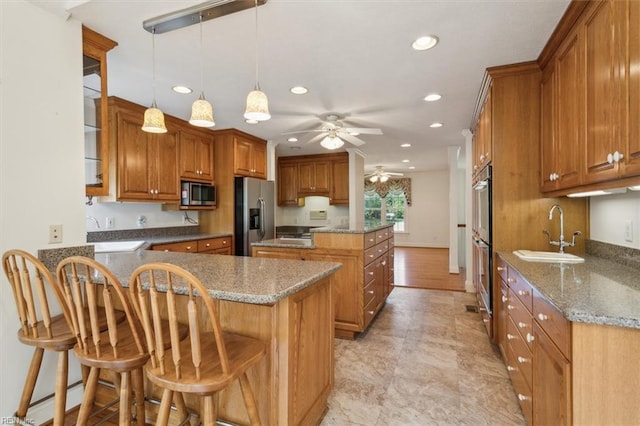 kitchen with a kitchen bar, stainless steel appliances, kitchen peninsula, sink, and ceiling fan