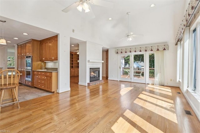 living area with a ceiling fan, visible vents, high vaulted ceiling, light wood-style flooring, and a brick fireplace