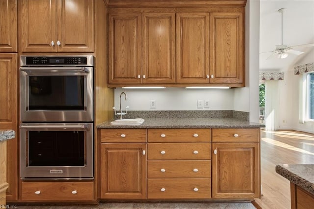 kitchen with vaulted ceiling, light hardwood / wood-style floors, ceiling fan, sink, and stainless steel double oven