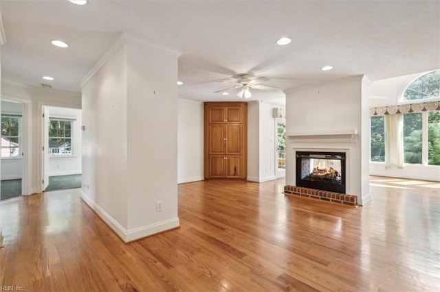 unfurnished living room with light hardwood / wood-style floors, a brick fireplace, ceiling fan, and a healthy amount of sunlight