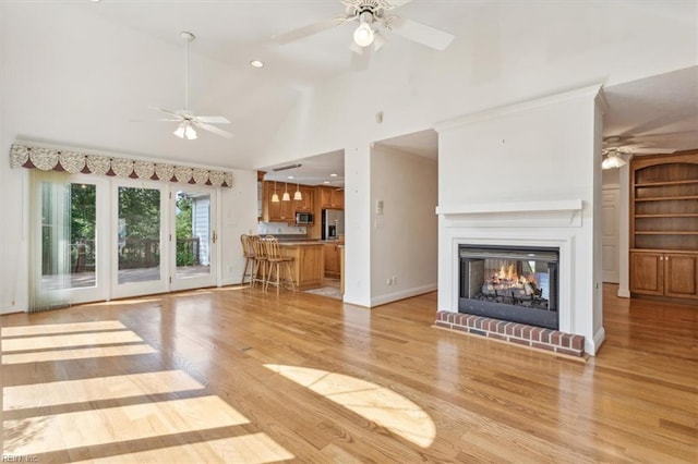 unfurnished living room with high vaulted ceiling, ceiling fan, light hardwood / wood-style floors, and a brick fireplace