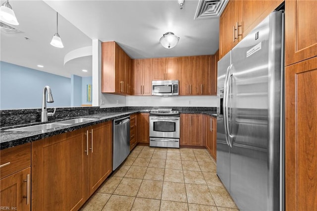 kitchen featuring brown cabinets, appliances with stainless steel finishes, light tile patterned flooring, a sink, and dark stone countertops