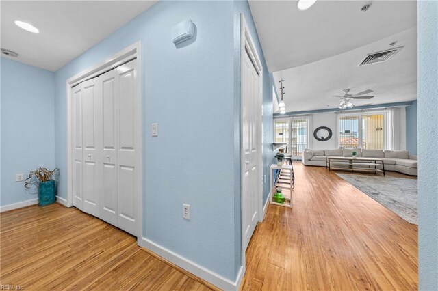 hallway with baseboards, visible vents, and wood finished floors