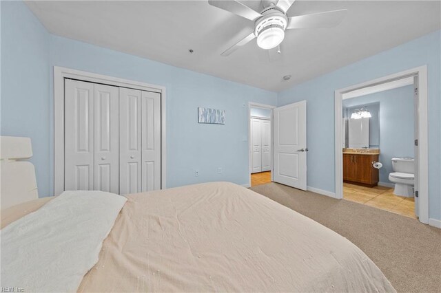 carpeted bedroom featuring a closet, ceiling fan, ensuite bath, and baseboards