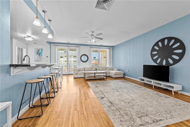 living area featuring light wood-type flooring, baseboards, visible vents, and a ceiling fan