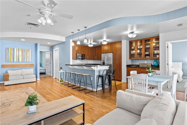 living room with a ceiling fan, visible vents, light wood-style flooring, and baseboards