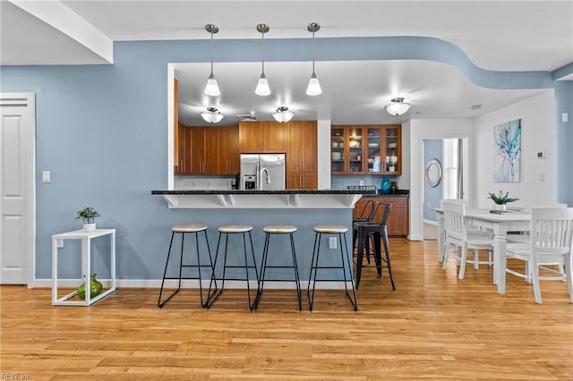 kitchen featuring light wood-style flooring, a breakfast bar, brown cabinets, a peninsula, and stainless steel refrigerator with ice dispenser