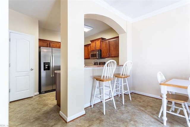 kitchen featuring baseboards, brown cabinetry, arched walkways, appliances with stainless steel finishes, and a kitchen breakfast bar