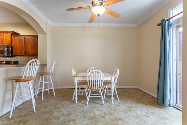 dining room featuring baseboards, arched walkways, ceiling fan, and ornamental molding