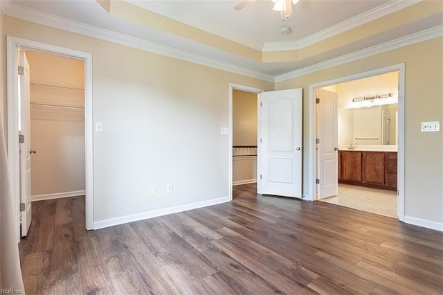 unfurnished bedroom with a tray ceiling, baseboards, a walk in closet, and wood finished floors