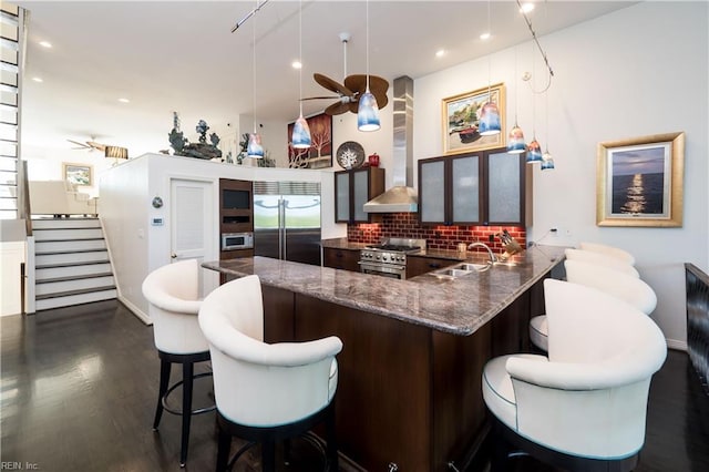 bar featuring high end appliances, sink, wall chimney range hood, ceiling fan, and tasteful backsplash