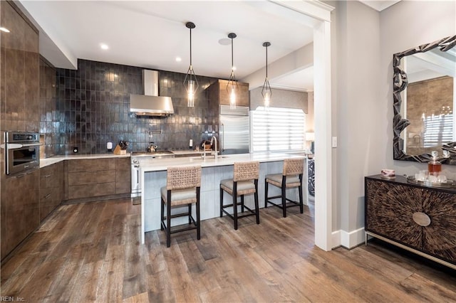 kitchen featuring dark wood-type flooring, stainless steel appliances, a kitchen breakfast bar, and wall chimney range hood