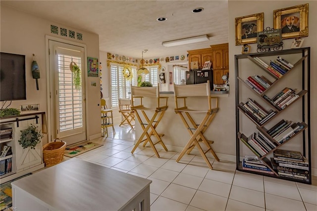 interior space with light tile patterned floors, brown cabinets, freestanding refrigerator, and decorative light fixtures