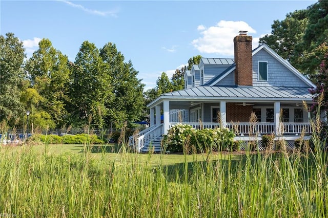 back of property featuring metal roof, a porch, a chimney, and a standing seam roof