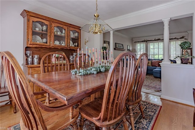 dining area with a chandelier, decorative columns, light wood finished floors, and ornamental molding