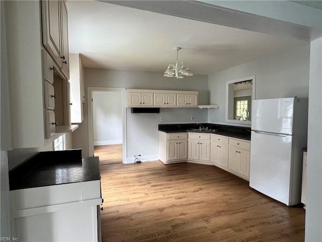 kitchen with wood-type flooring, sink, a notable chandelier, and white fridge