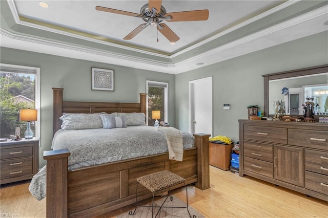 bedroom with a tray ceiling, ceiling fan, crown molding, and light hardwood / wood-style flooring