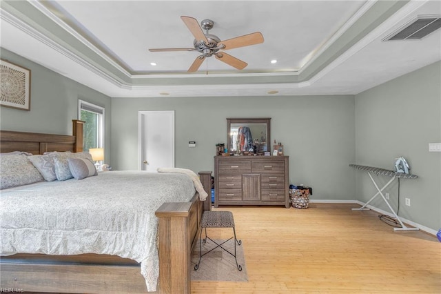 bedroom with crown molding, light hardwood / wood-style flooring, ceiling fan, and a raised ceiling