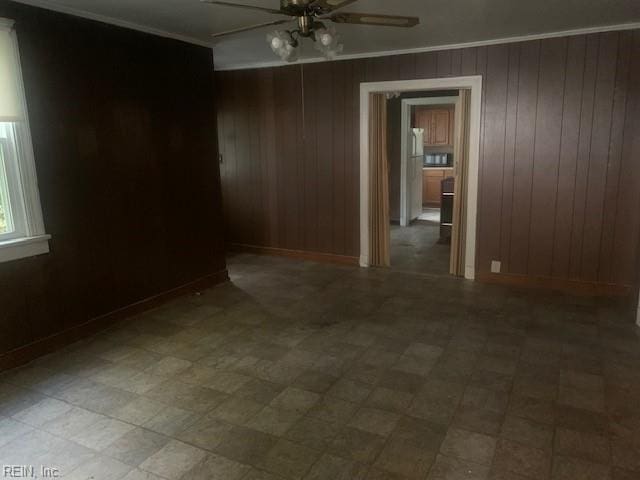 empty room featuring crown molding, ceiling fan, and wood walls