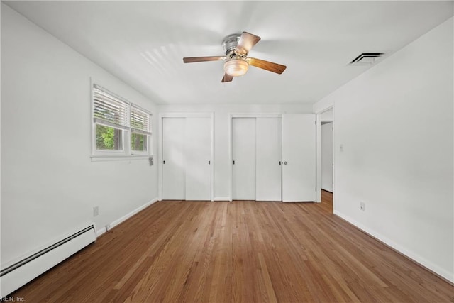 unfurnished bedroom with light hardwood / wood-style flooring, baseboard heating, multiple closets, and ceiling fan