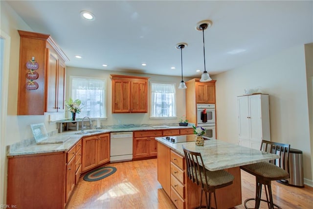 kitchen featuring a kitchen breakfast bar, white appliances, hanging light fixtures, a center island, and light wood-type flooring