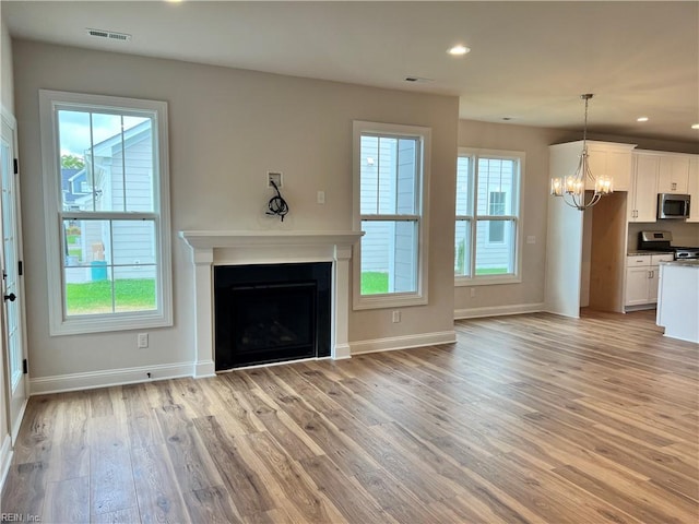 unfurnished living room with a chandelier, a wealth of natural light, and light hardwood / wood-style floors