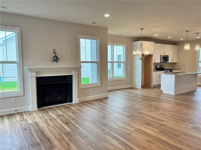 unfurnished living room featuring a chandelier, sink, and light hardwood / wood-style floors