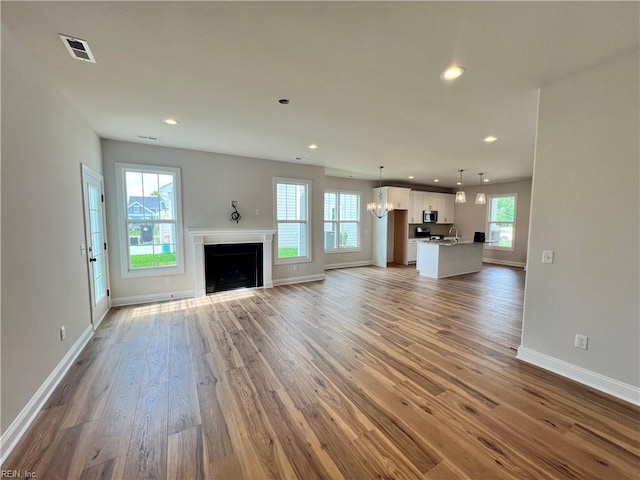 unfurnished living room with hardwood / wood-style flooring, an inviting chandelier, and a wealth of natural light