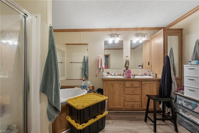 full bathroom featuring a sink, a textured ceiling, wood finished floors, a shower stall, and double vanity