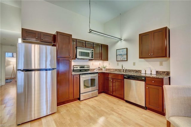 kitchen featuring stone counters, stainless steel appliances, light hardwood / wood-style floors, sink, and a towering ceiling