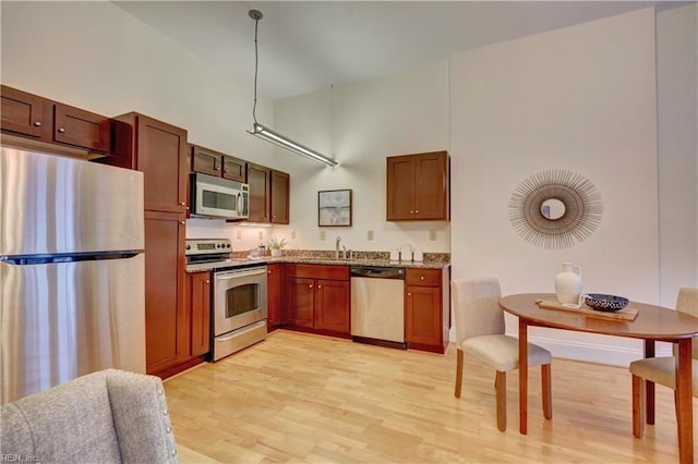 kitchen with a towering ceiling, appliances with stainless steel finishes, sink, and light hardwood / wood-style flooring