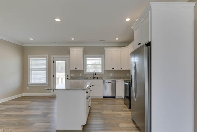 kitchen featuring light wood-type flooring, a center island, light stone countertops, appliances with stainless steel finishes, and white cabinets