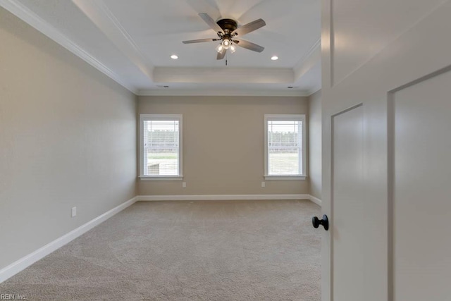 empty room featuring ceiling fan, a raised ceiling, light carpet, and ornamental molding