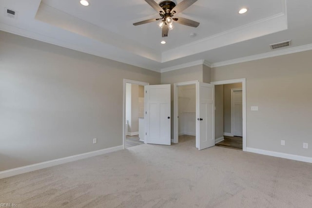 unfurnished bedroom featuring crown molding, a raised ceiling, a walk in closet, and ceiling fan