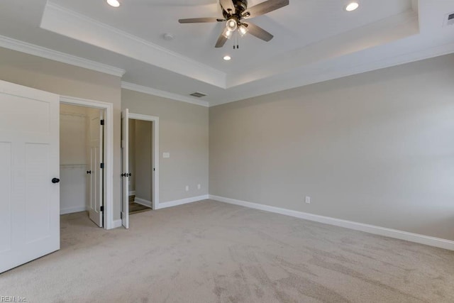 unfurnished bedroom with light carpet, ornamental molding, ceiling fan, a raised ceiling, and a spacious closet