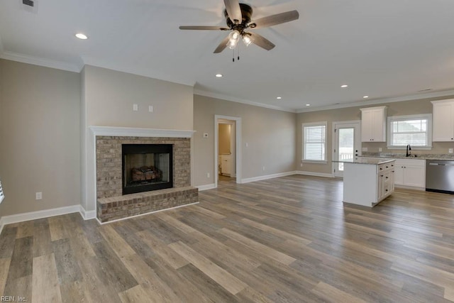 unfurnished living room featuring crown molding, ceiling fan, light wood-type flooring, and a fireplace