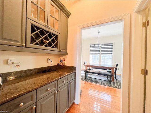 kitchen with ornamental molding, light wood-type flooring, and dark stone counters