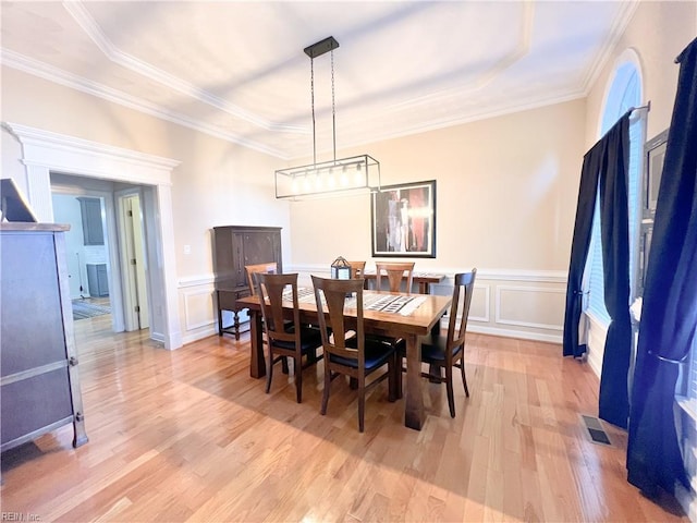 dining area with crown molding, a raised ceiling, and light hardwood / wood-style flooring