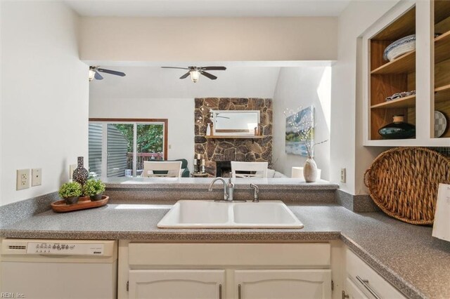 kitchen featuring white cabinetry, sink, white dishwasher, ceiling fan, and a stone fireplace