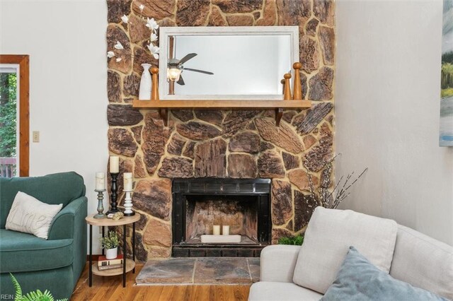 living room with wood-type flooring, ceiling fan, and a stone fireplace