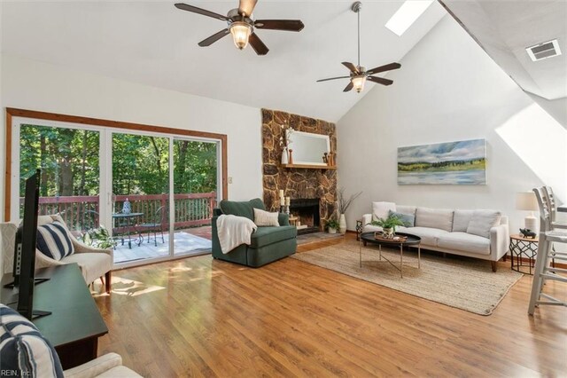 living room featuring a fireplace, high vaulted ceiling, hardwood / wood-style floors, a skylight, and ceiling fan