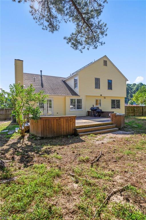 back of property with a deck, a shingled roof, fence, and a chimney